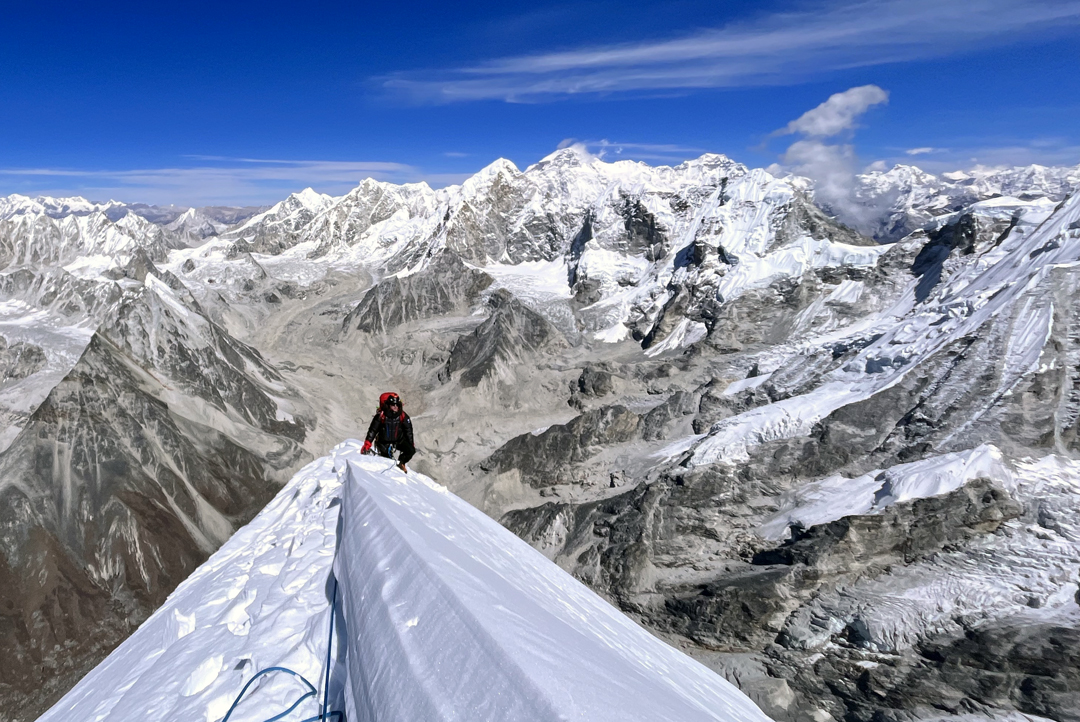 Maciej Kimel on the summit ridge of Chobutse. Below is the upper Rolwaling Glacier, while in the distance lie the Lunag Group, Cho Oyu, and Gyachung Kang.