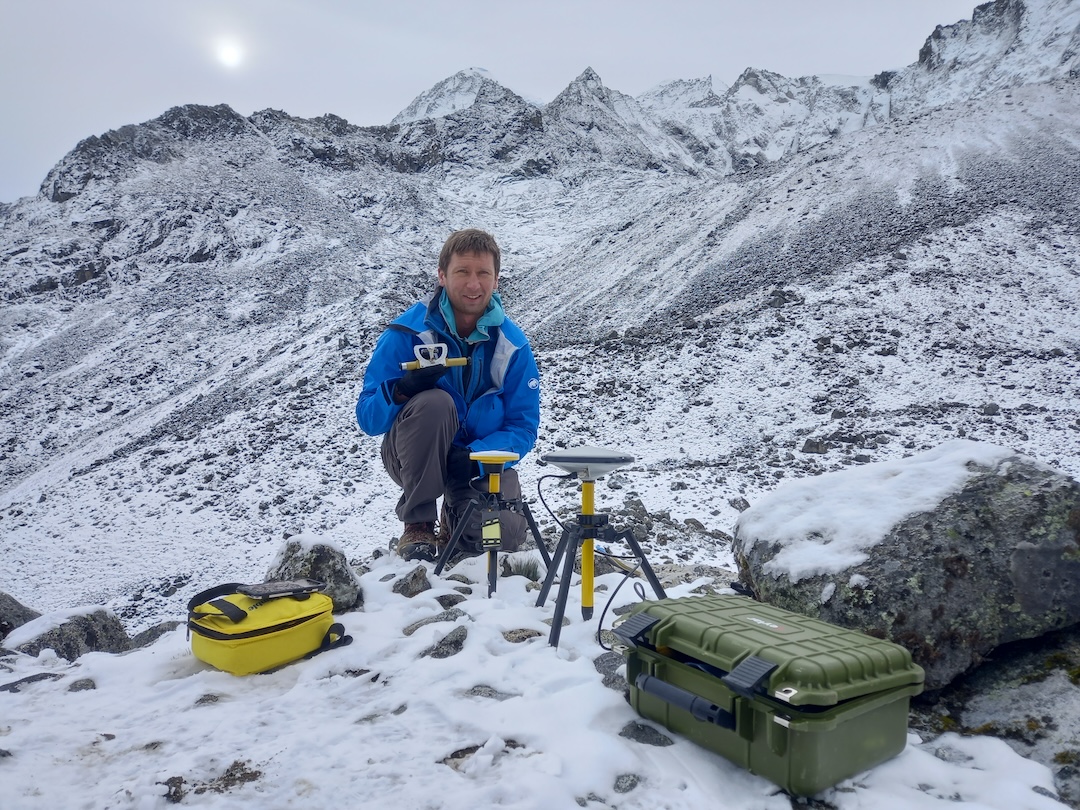 Eric Gilbertson with the survey equipment set up at base camp: an Abney level, Promark 220 dGPS with Ashtech antenna, and DA2 dGPS. Pico Cristóbal Colón (left) and Pico Simón Bolívar (right) are visible in the background. 

