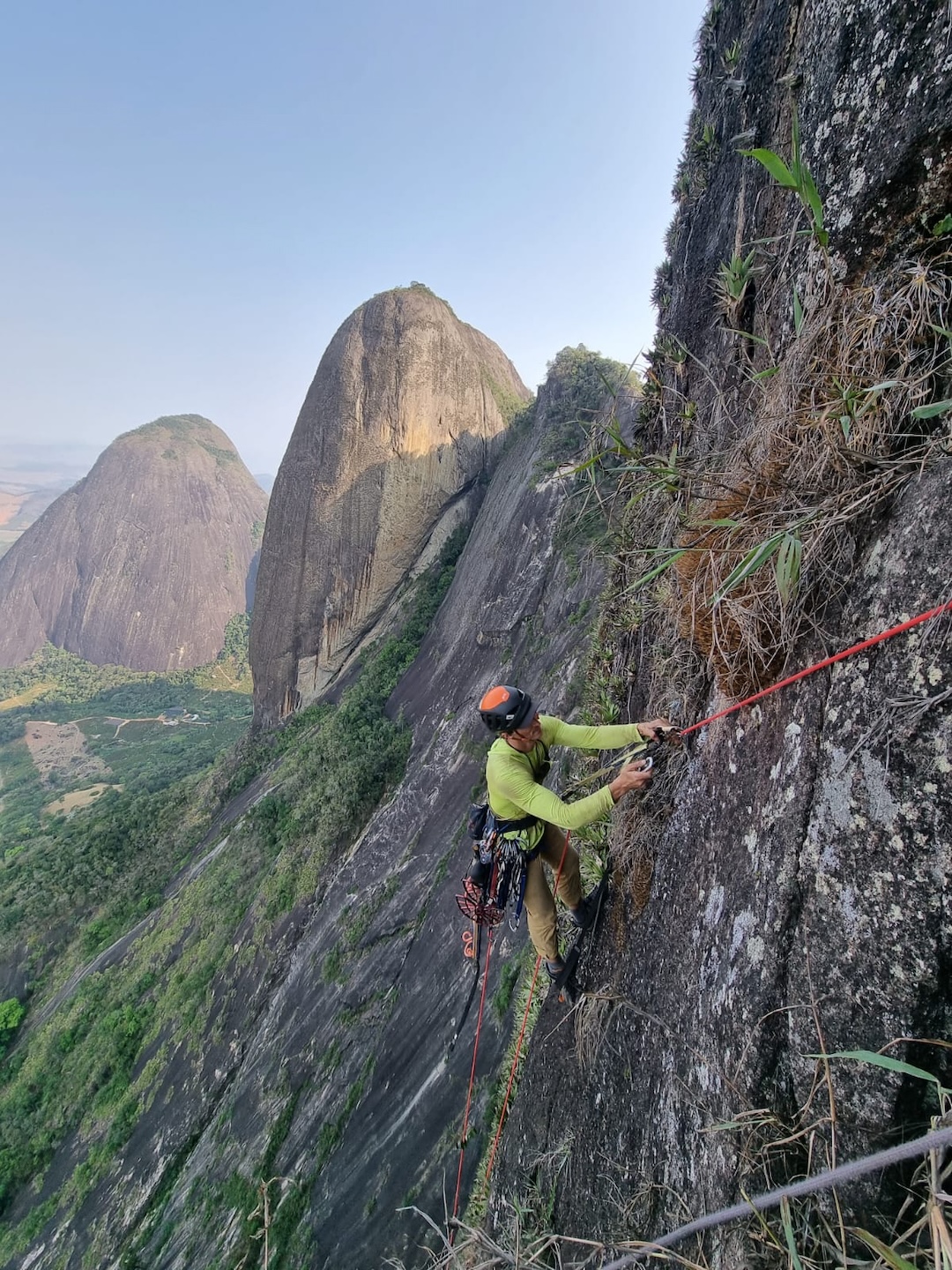 Willian Lacerda jugging the seventeenth pitch of the east face of Pedra do Cabrito. Behind Lacerda is Pedra do Fio. Further back, to the left, is Pedra Bicuda, another formation with walls roughly 1,000m in height, and only one existing route. 