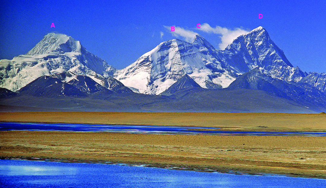Seen from the shores of Ram Tso and rising abruptly out of the Tibetan Plateau, the main peaks along the frontier ridge between China and Bhutan are: (A) Jitchu Drake (6,793m); (B) Chomolhari III (6,706m), with the north spur, climbed in 2025 for the first ascent of the peak, facing the camera; (C) Chomolhari II (6,972m); and (D) Chomolhari (7,326m). The elegant northwest ridge of Chomolhari, dropping steeply right from the summit, was climbed in 2006. 
