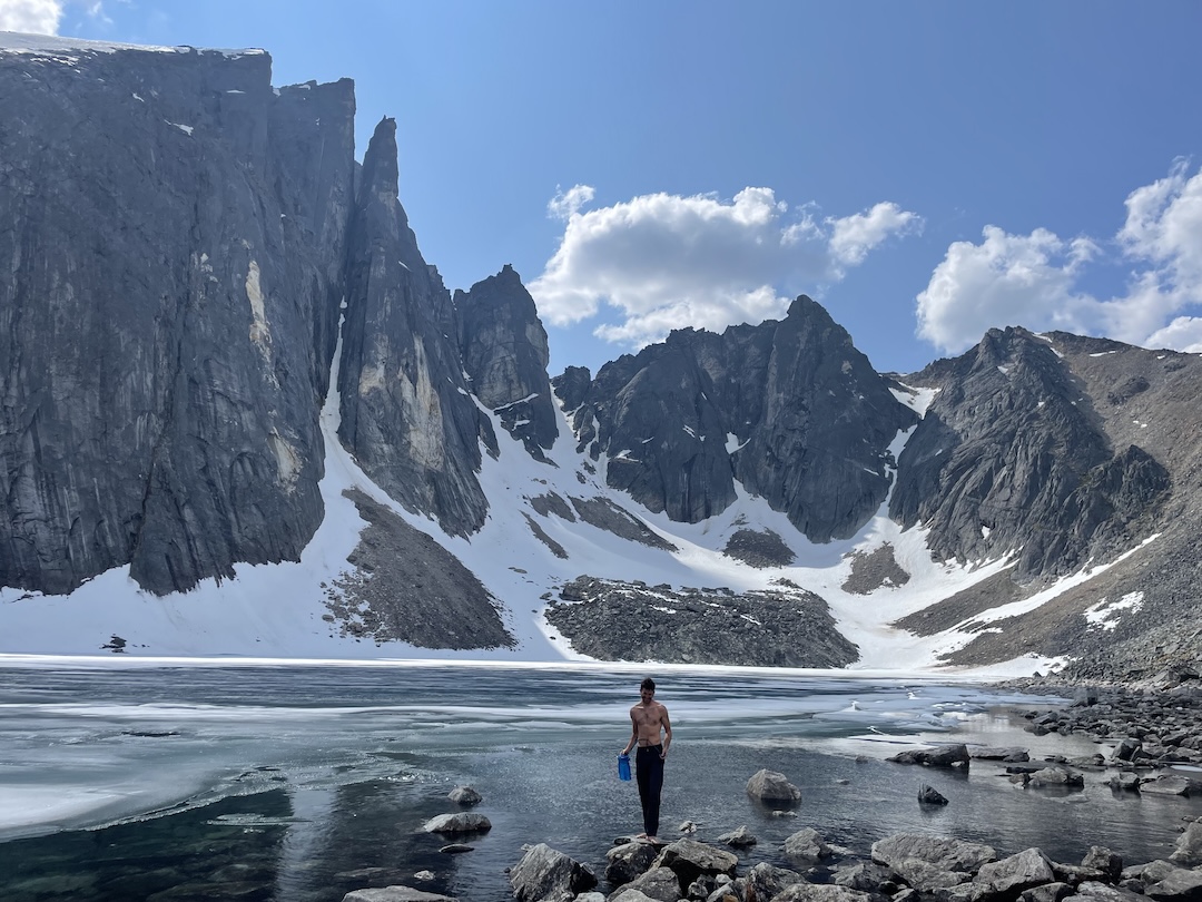 Dakota Walz filling water at the tarn below the Mosquito Pass Wall. Unikkiga Akłunaaq takes the obvious weakness left of the rightmost yellow streak.