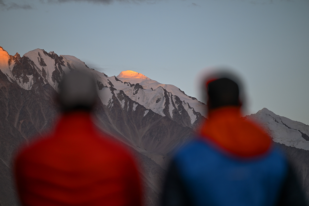 Lukas Woerle and Aleš Česen on the Khurdopin Glacier, a few kilometers from base camp. Cherireen Sar (6,224m GPS), seen between them, catches the sun. The west ridge, climbed in 2025, is its right skyline. The peak on the far right is an unclimbed subsummit on the ridge southwest of Khurdopin Sar. 