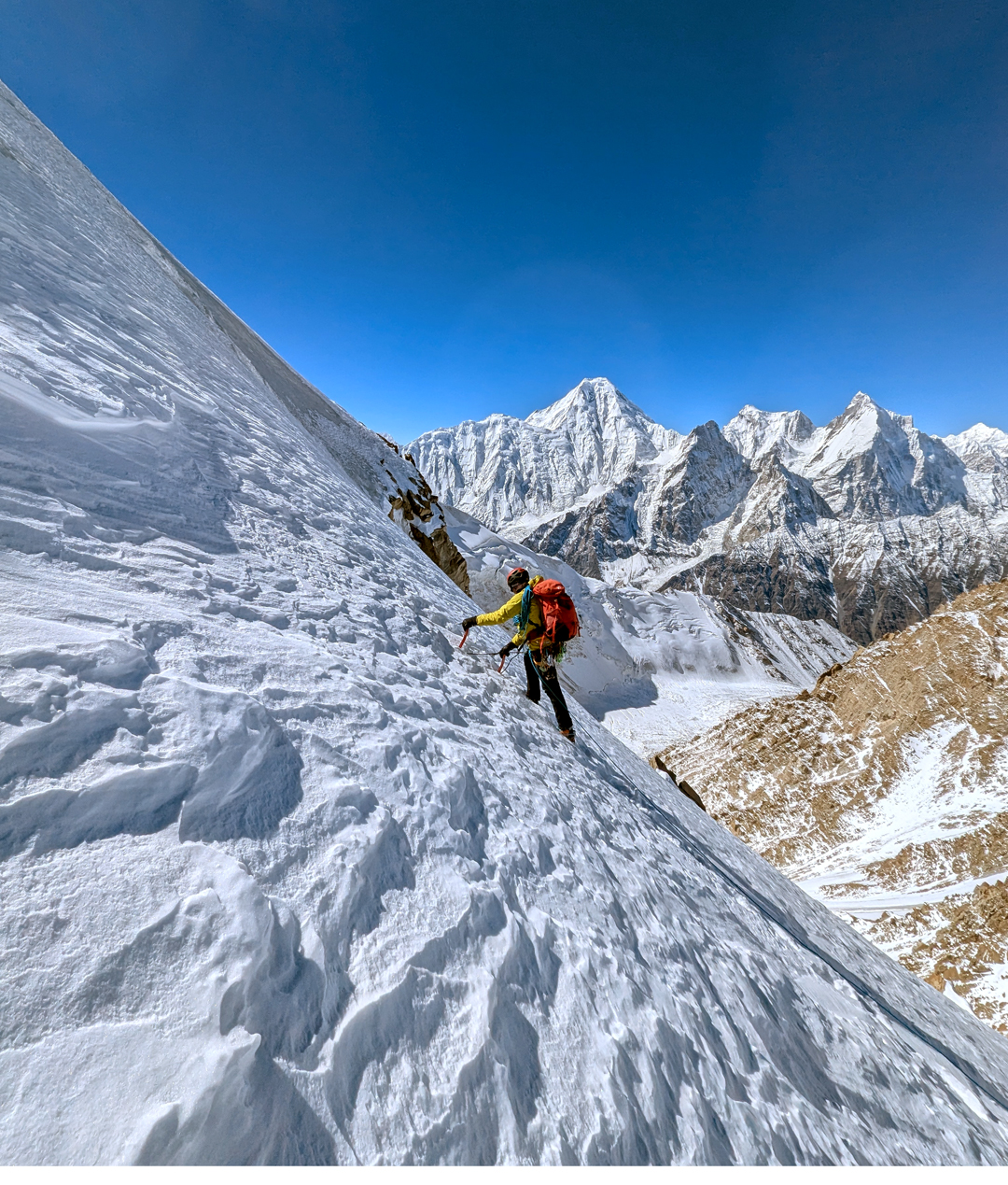 On the south face of Khurdopin Sar. The large peak above the climber is Kanjut Sar (7,760m), and the pointed peak on the right is Yukshin Gardan Sar (7,641m).