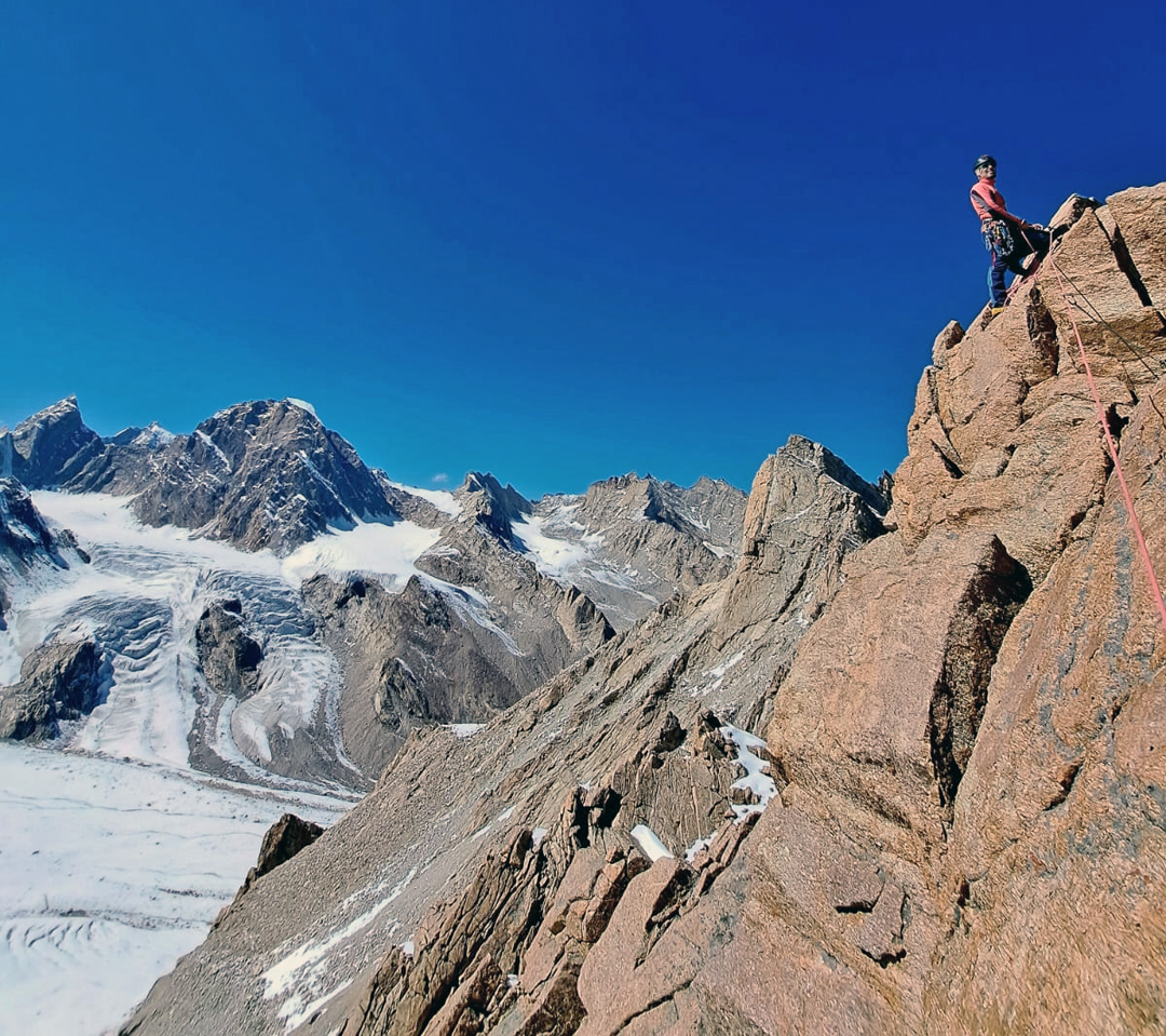 Alberto Urtasun atop the summit pinnacle of Peak 5,660m on the eastern rim of the Denyai Tokpo. The high, rounded summit behind and to the left is Khang Chan Chenmo (6,135m), climbed by the 2025 Dutch expedition. The pointed peak to the left is unclimbed.