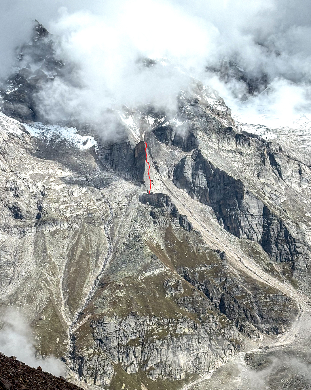 Temptation Tower, with the line of Etta (500 meters of climbing, 5.10 R), seen over the Duhangan Valley. Above, mostly hidden in cloud, is Peak 5,605m, while on the far right, peaking through the clouds, are the rocky flanks of the south face of Deo Tibba.  