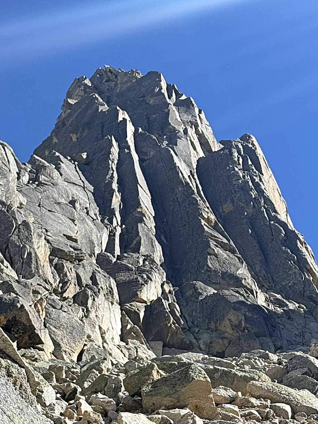 The south face of the Fourth Pillar of Ray Peak. There are three prominent dihedrals with their right walls in shadow. The 2025 route climbed splitter cracks up the sunny left wall of the third dihedral (farthest to the right), finishing with a long pitch up the southwest face directly to the summit.