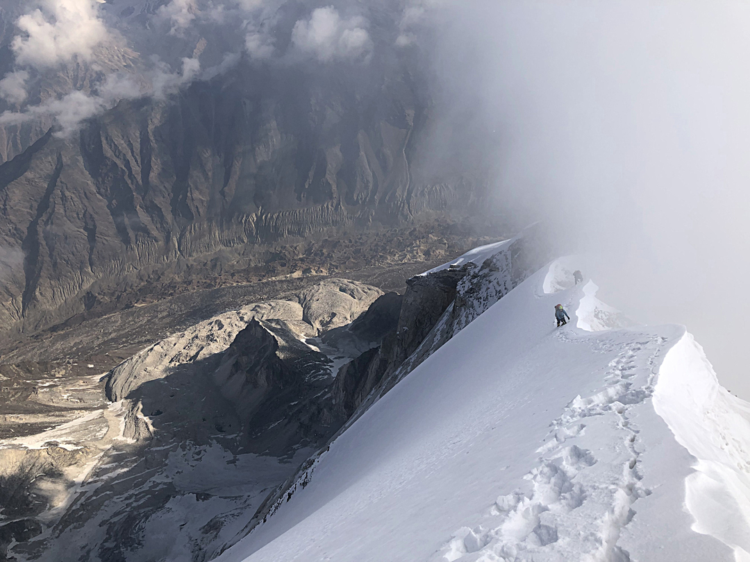 Magdalena Ritzau and Simon Schiefer on the final knife-edge ridge leading to the summit of Bhagirathi II, with the north face dropping steeply left toward the remains of the now receded Chaturangi Glacier far below. 