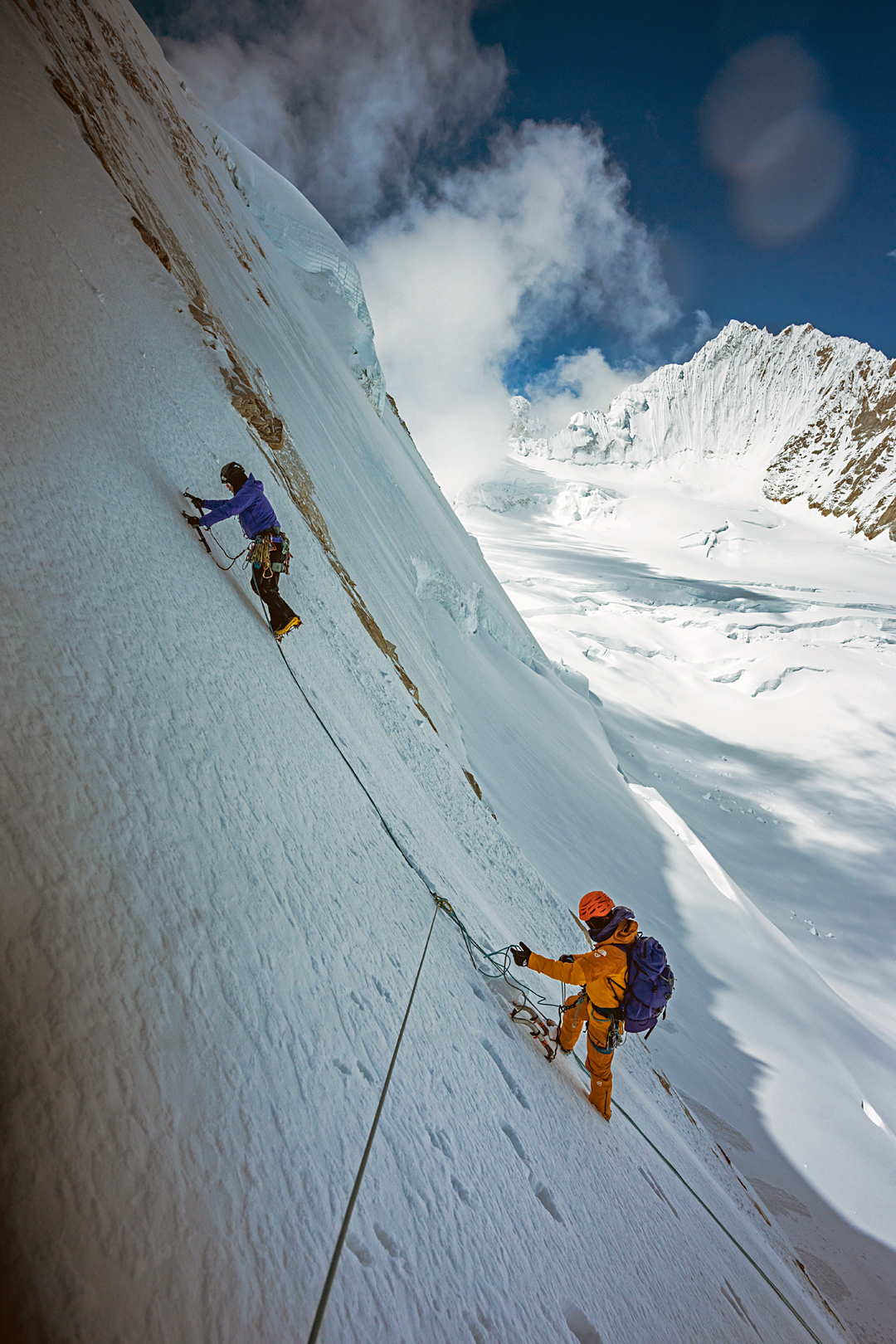 Huang Siyuan and Tong Haijun on the northwest face of Kangmi Kangri. Behind in the distance is the unclimbed northeast face of Karjiang (7,221m).
