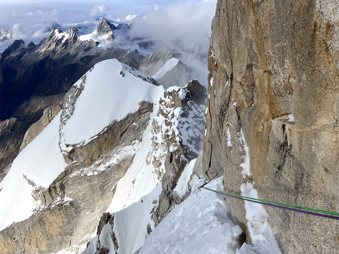 Looking back across the west flank of the north ridge of Siguniang. The snow-covered summit immediately behind is Siguniang North (5,900m). The first ascensionists climbed the ice couloir right of the granite walls, then up the sharp snow arête to finish. The distant rock pyramid is Yangmantai (5,666m), while the two summits to the left form the twin-summited Camel Peak (5,484m).