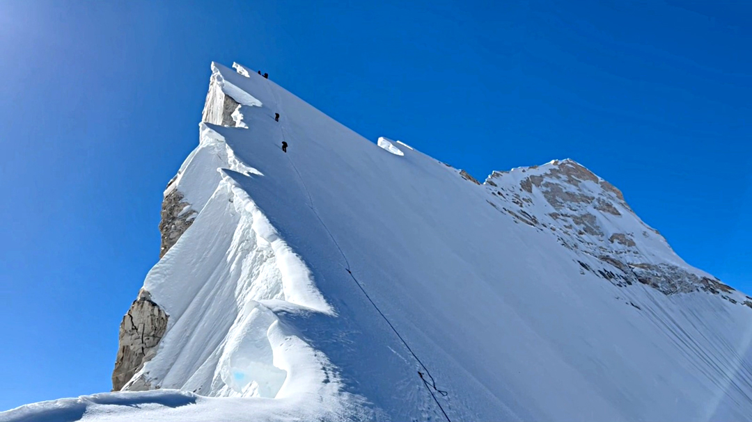 Heading up the north-northwest ridge of Meru (main summit on the right) from near the col below Meru Central. The climbers reached the snowy summit just catching the sun to the right. The 2006 Singleman/Swan jump site was immediately below and to the left of the upper two climbers.  
