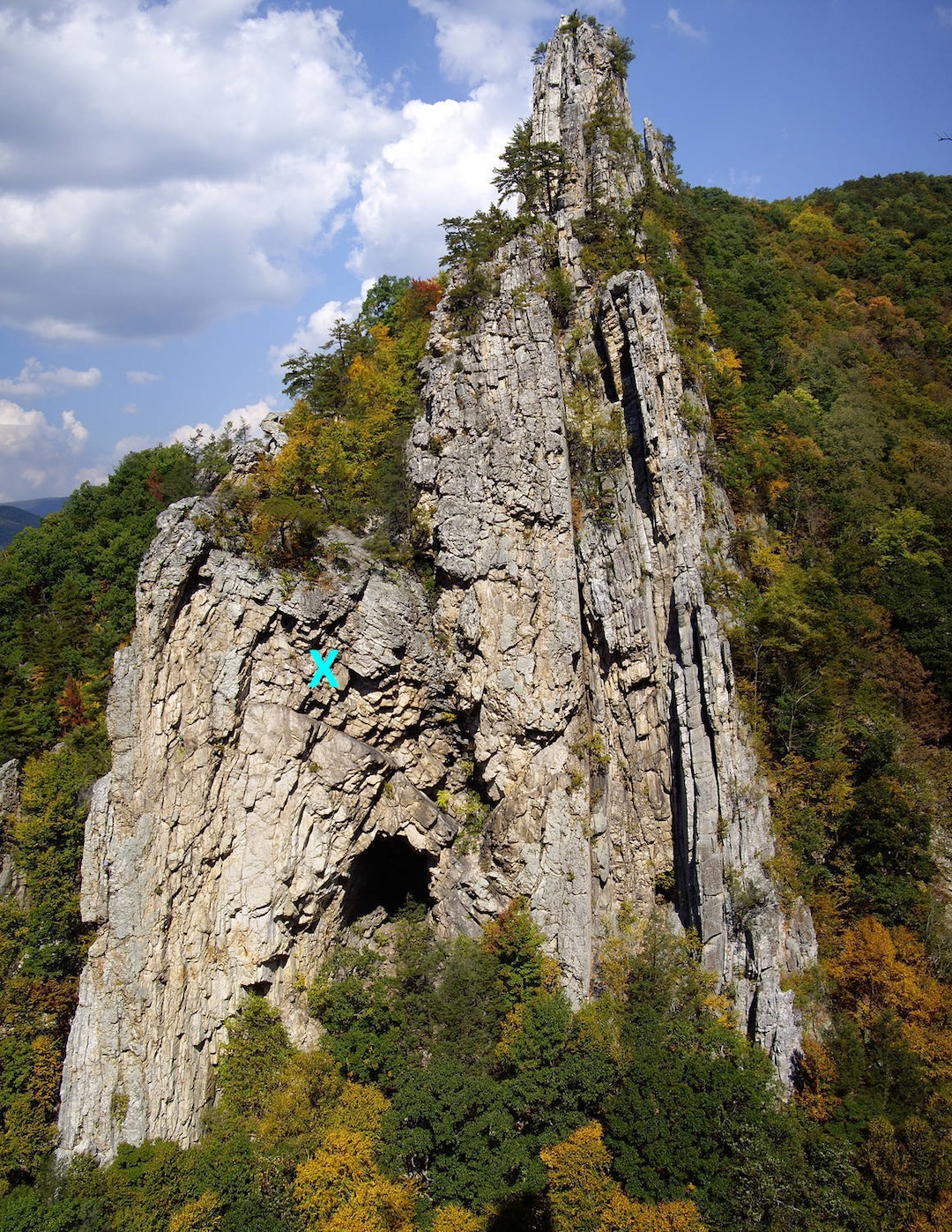 The third and final pitch of Simple J Malarkey climbs through the overlaps and triangular roofs seen here rising above and slightly left of the prominent cave. This pitch was the scene of a fatal rope-cutting accident (marked with a  blue X) in August 2023. 